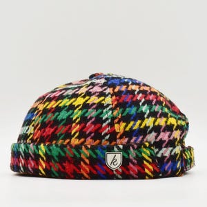 May include: A colorful, patterned beanie hat. The hat features a houndstooth design in black, red, yellow, green, pink, and blue. A small white label with a stylized "k" is sewn on the front. The hat is a stylish accessory.