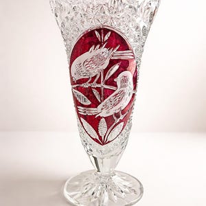 Könnte beinhalten: Transparente Kristallvase mit ausgestelltem Oberteil und Sockel. Die Vase hat eine rote ovale Tafel mit geätzten weißen Vögeln und Blättern. Das Kristall ist mit einem Sternmuster auf dem Sockel und einem strukturierten Rand geschnitten.