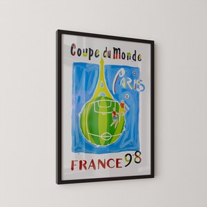 May include: Framed poster with a black border. The artwork features a green soccer ball with a field design, two figures playing soccer, and the Eiffel Tower. Text includes "Coupe du Monde", "Paris", and "France 98".
