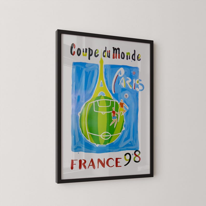 May include: Framed poster with a black border. The artwork features a green soccer ball with a field design, two figures playing soccer, and the Eiffel Tower. Text includes "Coupe du Monde", "Paris", and "France 98".