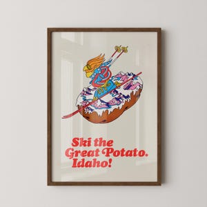 May include: A framed poster with a retro illustration of a potato with a skier. The skier is depicted as a bird wearing a blue and red outfit, skiing down a snowy mountain. The text "Ski the Great Potato. Idaho!" is in red.