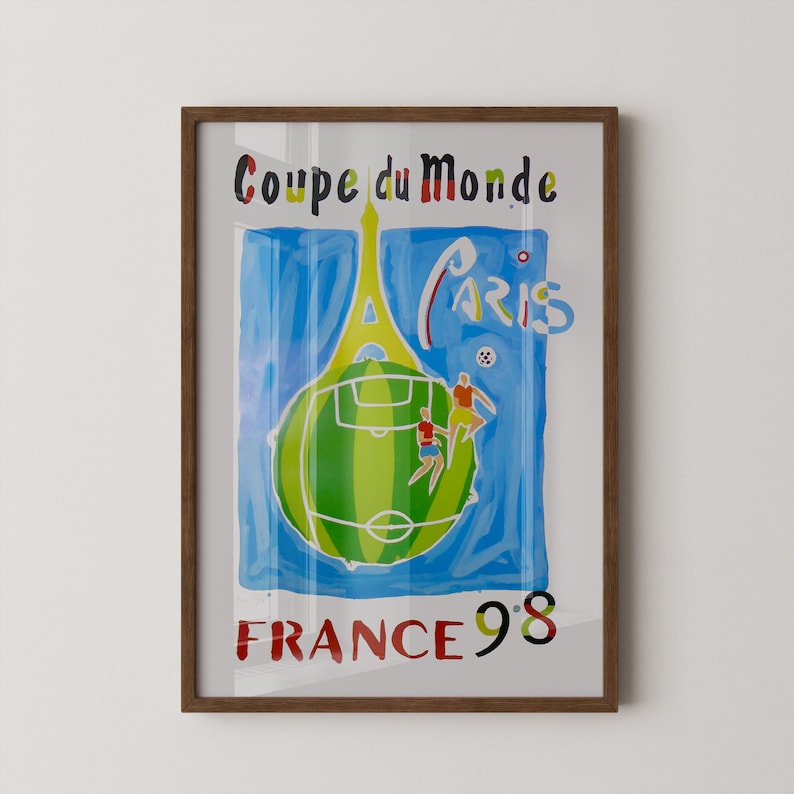 May include: Framed art print with a vibrant illustration for the 1998 FIFA World Cup in France. The artwork depicts the Eiffel Tower, a football pitch, and the text "Coupe du Monde Paris France 98."