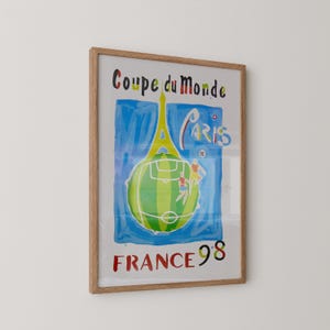 May include: Framed poster with a vibrant illustration for the 1998 FIFA World Cup in France. The design includes the Eiffel Tower, a football pitch, and the text "Coupe du Monde Paris France 98."