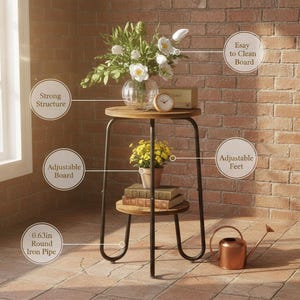 K&ouml;nnte beinhalten: Kleiner, runder Beistelltisch aus Holz mit schwarzem Metallrahmen. Der Tisch hat zwei Ebenen mit einem Regal darunter. Auf der Tischplatte stehen eine Vase mit wei&szlig;en Blumen, eine kleine Uhr und eine kleine Topfpflanze. In der N&auml;he einer Backsteinmauer.