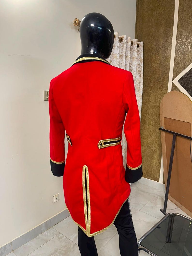 May include: A bright red tailcoat jacket featuring black cuffs and a black collar. The garment is accented with gold piping along the collar, the back waist pockets, and the central back vent. The jacket has a long, structured tail design.