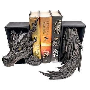 May include: Black dragon-themed bookends with three books. The dragon head and tail bookends are on either side of the books. The books are titled "Fourth Wing", "Iron Flame", and "Onyx Storm" by Rebecca Yarros.