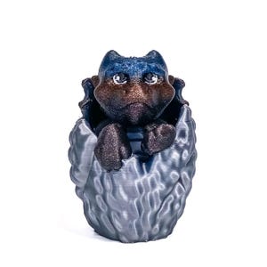 May include: A 3D-printed figurine of a small, dark-colored creature with large ears and a grumpy expression, nestled inside a textured, egg-like structure. The creature has blue and brown accents.
