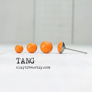 May include: Four orange round stud earrings of different sizes. The largest earring is on a silver post.