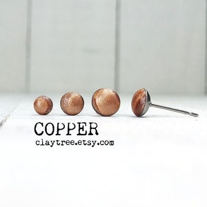 May include: Four copper-coloured stud earrings of varying sizes, with the smallest on the left and the largest on the right. The largest earring has a silver post.