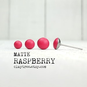 May include: Four matte raspberry coloured polymer clay earrings, the largest one is on a silver post. The earrings are arranged in a line from smallest to largest. The text "MATTE RASPBERRY claytree.etsy.com" is below the earrings.