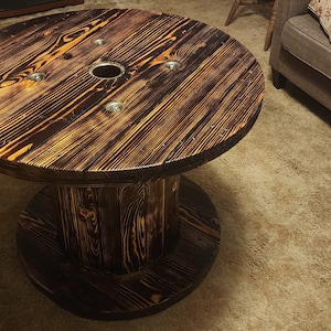 May include: A round, rustic coffee table made from a repurposed wooden cable spool. The table features a dark brown stained finish with visible wood grain and metal hardware. The table is approximately 36 inches in diameter and 20 inches tall.