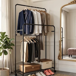 May include: A black metal clothing rack displays a navy blazer, white shirts, and other garments on wooden hangers. Below, pants, a leather jacket, and two wooden storage boxes are visible. Shoes and slippers are arranged on the floor.