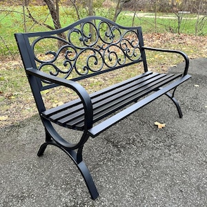 May include: A black metal garden bench with a decorative back and armrests. The bench features a slatted seat and ornate scrollwork on the backrest. The bench is designed for outdoor use and is made of durable metal.