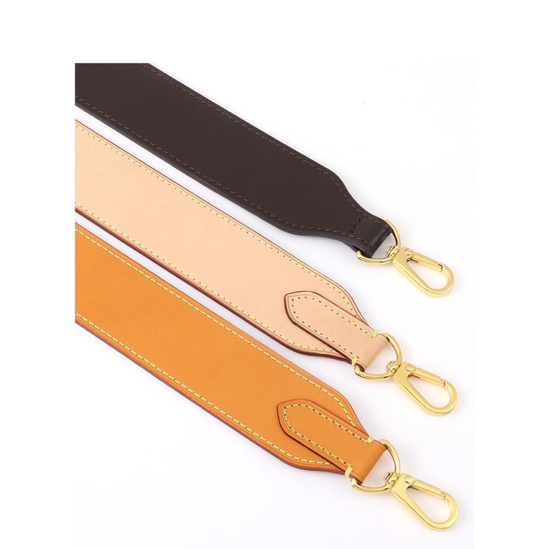 May include: Three leather bag straps in brown, tan, and orange, each with gold-colored metal clasps. The straps are stitched with a contrasting thread and are angled across a white background.