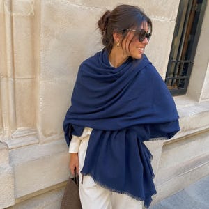Peut inclure: Une grande écharpe rectangulaire bleu marine avec une finition douce et texturée et des bords effilochés. L'écharpe est drapée lâchement sur les épaules, mettant en valeur sa grande taille et son tissu léger qui tombe en plis souples.
