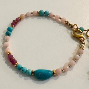 May include: A turquoise and pink beaded bracelet with a gold clasp. The bracelet features a large turquoise gemstone.