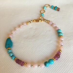 May include: A gold bracelet with pink, turquoise, and purple beads. The bracelet has a lobster clasp closure.