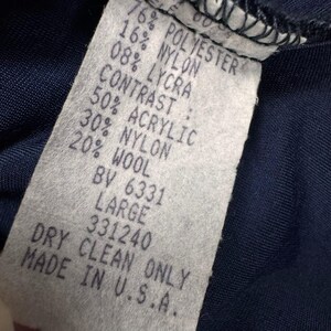 May include: A close-up of a clothing label with text detailing the fabric composition. The label states: 76% POLYESTER, 16% NYLON, 08% LYCRA, CONTRAST: 50% ACRYLIC, 30% NYLON, 20% WOOL, LARGE, DRY CLEAN ONLY, MADE IN U.S.A.