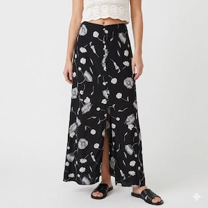 May include: Black floral print skirt with a button-down front and a front slit. The skirt features a pattern of white flowers and leaves. The skirt is a maxi length.