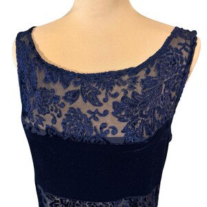May include: A navy blue sleeveless dress with a sheer, embroidered floral overlay. It features a velvet band across the chest and a scoop neckline. The intricate design and dark colour give it an elegant appearance.