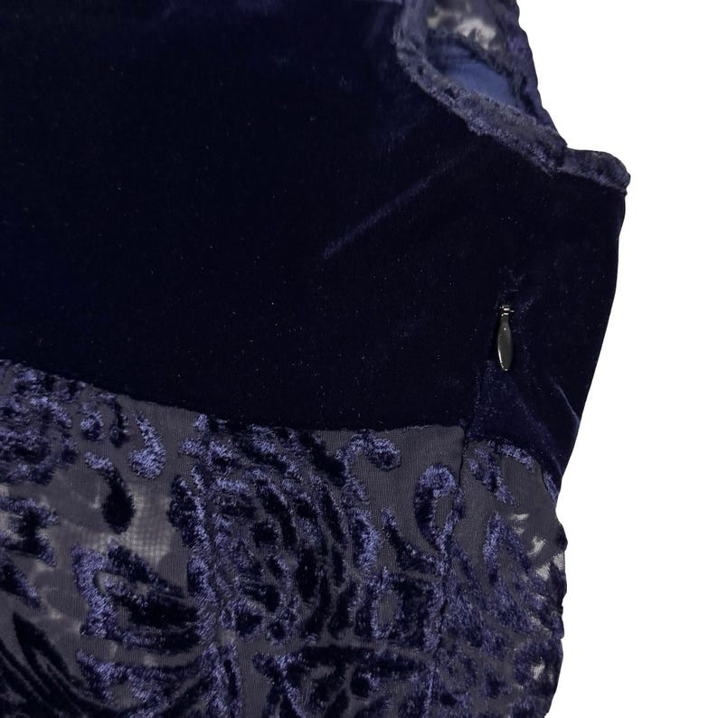 May include: A white ceramic mug with a black handle and the text "But First, Coffee" in a black, bold font. The mug is on a white surface. The mug is approximately 10 cm tall.