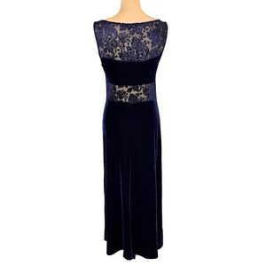 May include: A navy blue velvet gown featuring a sheer floral lace panel across the upper back and waist. The sleeveless dress has a floor-length skirt and a scoop neckline. This is a formal evening dress.