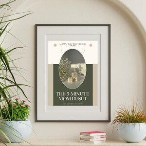 Könnte beinhalten: Gerahmter Druck mit dem Text "THE 5-MINUTE MOM RESET" in einem schwarzen Rahmen. Der Druck hat eine neutrale Farbpalette mit einem ovalen Design und den Worten "A SIMPLE DAILY RESET FOR BUSY MOMS" oben. Der Druck wird auf einem Holzregal angezeigt.