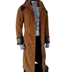 Peut inclure: Long manteau marron avec un col montant et des empiècements noirs sur les épaules et les manches. Le manteau a une coupe ajustée et comporte plusieurs poches et une fermeture boutonnée. Les manches ont des détails rayés marron et noirs.