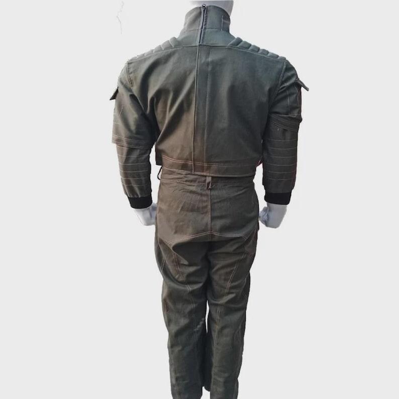 May include: A two-piece olive green jumpsuit with a high collar and a zipper down the front. The jacket has pockets on the sleeves and a cropped waist. The pants are straight-legged. The suit has black cuffs and is displayed on a mannequin.