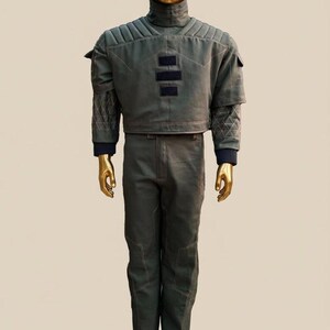 May include: A two-piece olive green outfit on a gold mannequin. The top has a high collar and quilted shoulder detail. The pants are straight-legged. The mannequin has a gold head and hands.