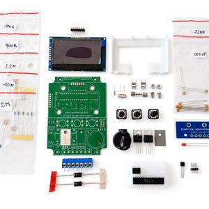May include: An electronic DIY irrigation controller kit featuring a green printed circuit board, a rectangular display module, three push buttons, various resistors in labeled plastic bags, capacitors, diodes, a battery holder, and a blue control panel label.
