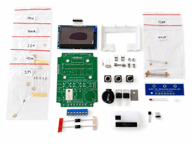 May include: An electronic DIY irrigation controller kit featuring a green printed circuit board, a rectangular display module, three push buttons, various resistors in labeled plastic bags, capacitors, diodes, a battery holder, and a blue control panel label.