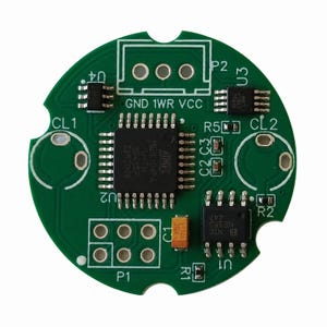 May include: A circular green printed circuit board featuring a central Atmel microcontroller, an 8-pin NE555 timer chip, and various surface-mount components. The board includes labeled connection points for GND, 1WR, and VCC, along with P1 and P2 headers.