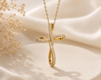 May include: A gold-toned necklace featuring a cross pendant with a twisted, fluid design. The surface of the cross is encrusted with small, clear, sparkling stones along the front. The pendant hangs from a delicate, thin gold-toned metal chain.