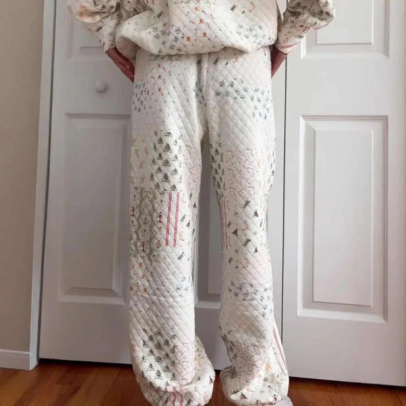 May include: Cream quilted trousers with a patchwork design. The trousers feature a diamond pattern and are adorned with embroidered trees and red stripes. The matching top is visible. The trousers are made of a soft, comfortable material.