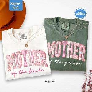 May include: Two Comfort Colors t-shirts, one ivory and one moss green, with the word "MOTHER" in pink floral patchwork letters. The ivory shirt says "of the bride" and the green shirt says "of the groom". Both shirts have a gold necklace.