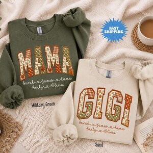 May include: A military green sweatshirt with the word MAMA and a sand sweatshirt with the word GIGI, both featuring patchwork-style letters in autumn colours. Below the words, the names Sarah, James, Emma, Emily, and Olivia are printed in script.