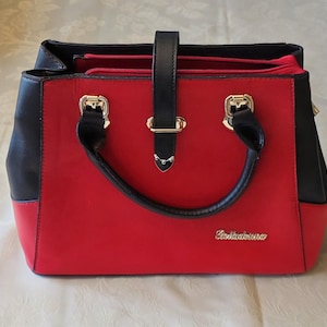 May include: A red and black handbag with a top handle and gold-colored hardware. The bag features a rectangular shape with a black top and sides, and a red front and bottom. The word "Belladonna" is written in gold script on the front.