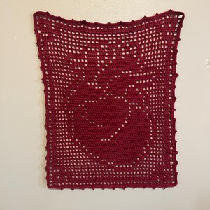 May include: A rectangular dark red crochet wall hanging featuring a detailed anatomical heart design created with a grid-like filet stitch pattern. The piece has a scalloped border along all four edges and is displayed flat against a plain wall.