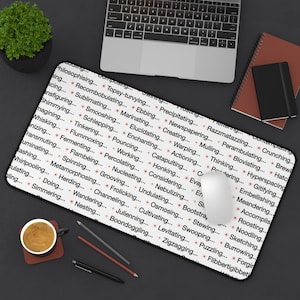 May include: A rectangular white mousepad with a black border, covered in a repeating pattern of words in a serif font. The words are in a reddish-brown color and are arranged in a grid-like fashion. A computer mouse, keyboard, and other office supplies are visible.