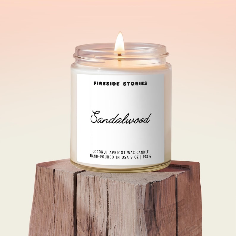 May include: A lit, clear glass jar candle labeled "FIRESIDE STORIES Sandalwood." The candle is hand-poured in the USA and contains coconut apricot wax. The candle is 9 oz (255 g).
