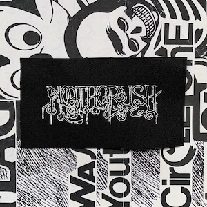 Può includere: Una toppa rettangolare nera con il testo bianco "NOTHERCRUSH" in un carattere gotico stilizzato. La toppa è posta su uno sfondo in bianco e nero con vari elementi grafici e testo.