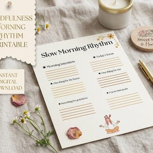 May include: A printable mindfulness morning rhythm worksheet with the text "Slow Morning Rhythm". The worksheet includes sections for intentions, focus, and gratitude. A pen, candle, and decorative items are also present.
