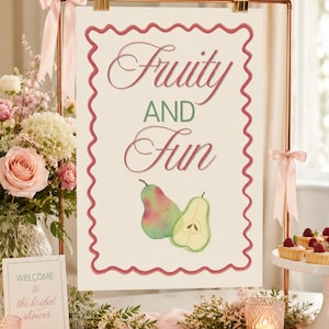 Peut inclure: Une affiche "Fruity and Fun" avec des poires aquarelles, encadrée de cuivre et ornée de rubans roses. La scène est décorée pour une fête prénuptiale, avec des fleurs et des pâtisseries.