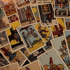 May include: A collection of vintage tarot cards, featuring illustrations and titles such as "The Devil," "Judgement," and "Knight of Pentacles." The cards are arranged in a scattered pattern, showcasing various artistic designs and colors.