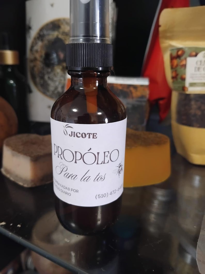 May include: A brown glass spray bottle with a black cap and a white label. The label reads "Jicote Prop&oacute;leo Para la tos". The bottle is filled with a light brown liquid. The background includes other products.