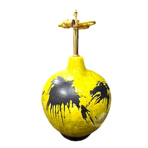 May include: A yellow ceramic table lamp with black abstract splatter paint design. The lamp has a brass base and a round, globe-shaped shade.
