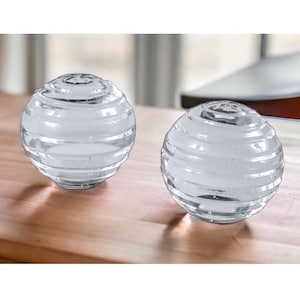 May include: Two clear glass spheres with a textured, ribbed surface. The spheres are sitting on a wooden surface.