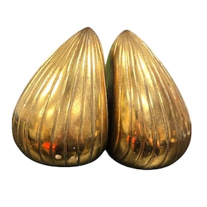 May include: Two gold-colored, teardrop-shaped objects with vertical ribbed detailing. The objects have a metallic sheen and are set against a white background. The design suggests a decorative or ornamental purpose.