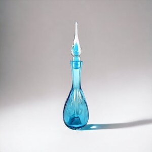 May include: A blue glass bottle with a clear glass stopper. The bottle has a rounded body and a long, thin neck. The stopper is shaped like a teardrop.